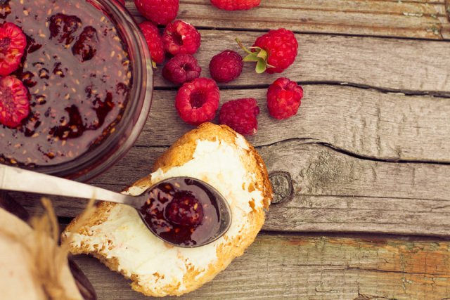 Raspberry jam in a jar and on toast, and fresh berries on the wooden table.