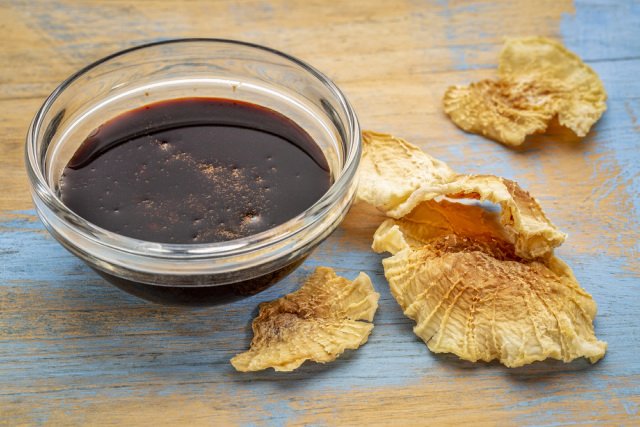 Yacon syrup in a bowl and dried Yacon slices on a wooden table.