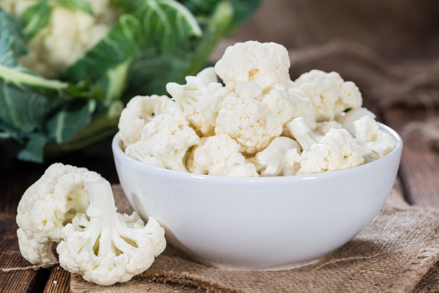 Freshly cut cauliflowers in a white bowl on a wooden table
